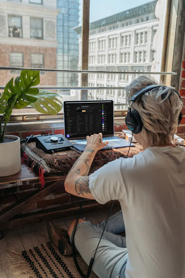 Productor musical con audífonos creando una pista instrumental en una laptop